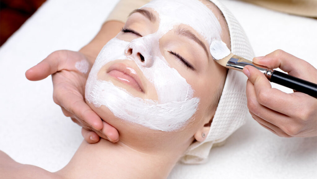 Woman with closed eyes having a facial spa treatment with a white mask applied with a brush.