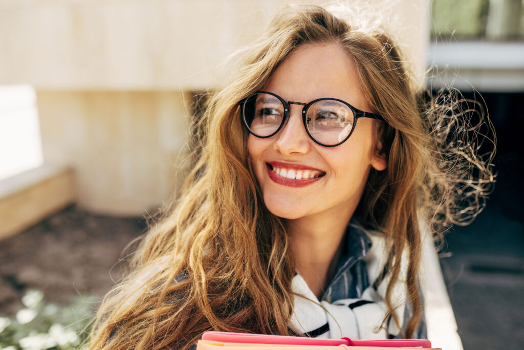 Smiling woman with long, wavy blonde hair wearing stylish round glasses with a dark frame.